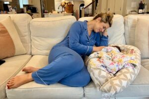 Lesley in blue pajamas cuddling with a newborn on the couch